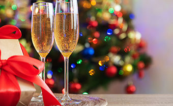 champagne glasses next to a gift box with a red bow and a christmas tree in the background